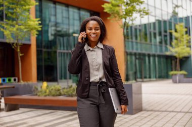 Modern bir şehir ortamında telefonda konuşurken gülümseyen kendine güvenen profesyonel bir kadın..