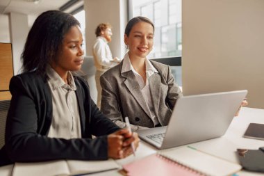 İki iş kadını, modern bir çalışma alanında takım çalışması ve yenilik sergileyen bir dizüstü bilgisayarda işbirliği yapıyorlar..