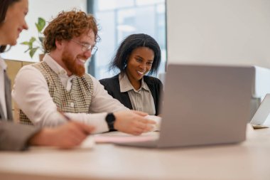 Çeşitli bir ekip, bir iş toplantısı sırasında laptoplarla verimli ve işbirlikçi bir tartışmaya girişiyor.