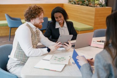 Ekip üyeleri, parlak ve davetkar bir çalışma alanında dijital cihazlar kullanarak verimli bir tartışmaya giriştiler.