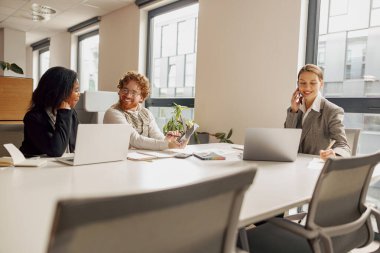 Üç kadın modern bir ofis masasında hevesle iş birliği yaparken verimli bir şekilde tartışıyorlar.