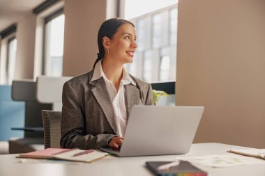 Kendini işine adamış ve işine odaklanmış profesyonel bir kadın laptopuyla şık ve modern bir ofis alanında meşgul.