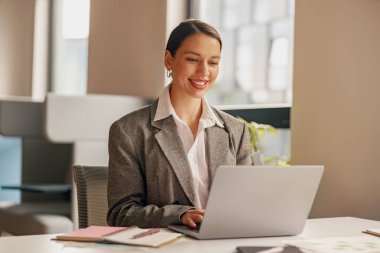 Profesyonel bir kadın, şık ve şık bir ofis ortamında dizüstü bilgisayarında çalışmaktan zevk alır.