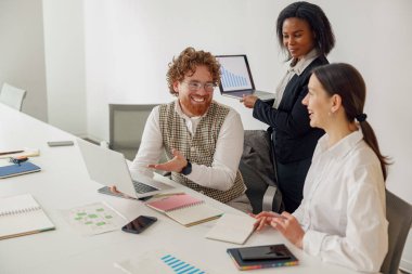 Aydınlık bir ofiste, çeşitli bir ekip laptopları kullanarak ve belgeleri tutarak hevesle işbirliği yapıyor.