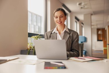 Kendini işine adamış ve işine odaklanmış profesyonel bir kadın modern ofis ortamında bir dizüstü bilgisayarla meşgul.