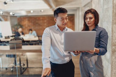 Çağdaş, modern bir ofis alanında dizüstü bilgisayarla iş birliği yapan meşgul ve motive olmuş profesyoneller.