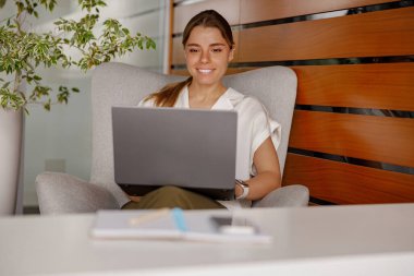 Parlak bir gülümsemesi olan genç bir kadın, görevlerini modern bir ofiste özenle yerine getiriyor.