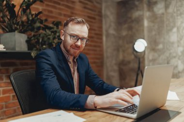 Çağdaş ofis ortamında özenle dizüstü bilgisayar üzerinde çalışan özel dikim takım elbiseli bir adam.