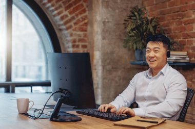 Rahat kulaklıklı bir adam şık bir ofiste çalışıyor tuğla duvarları ve modern bir bilgisayarı var.