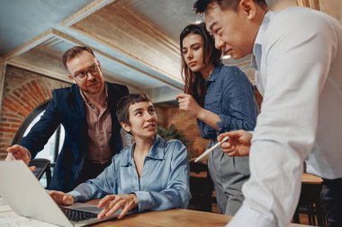 Çeşitli bir ekip, modern bir çalışma alanındaki bir dizüstü bilgisayarın üzerinde ortaklaşa beyin fırtınası yapıyor.