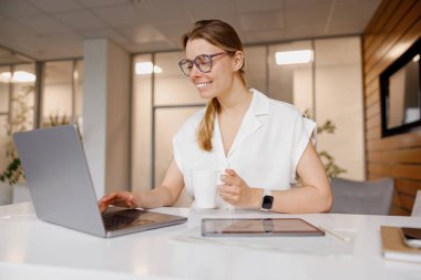 Genç bir profesyonel, enerjik ve hevesli, modern bir ofiste dizüstü bilgisayarıyla meşgul.