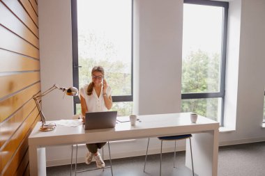 Parlak bir ofiste, odaklanmış genç bir kadın özenle dizüstü bilgisayarı üzerinde çalışır ve dikkat çekici bir üretkenlik gösterir.