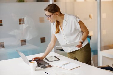 Kendini işine adamış bir kadın, modern, işbirlikçi ofis ortamında dijital cihazlarla çalışıyor.