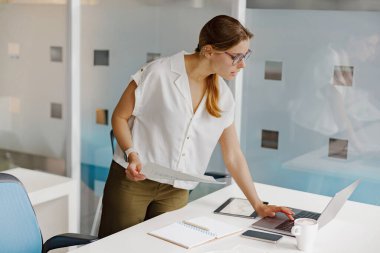 Modern teknolojiyle donatılmış şık bir ofis masasında önemli belgeleri derinden analiz eden odaklanmış bir kadın.