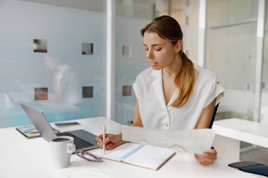 Şık, modern bir ofis ortamında, genç bir kadın çalışmalarına özenle bağlanıyor, yüksek üretkenliğini sergiliyor.