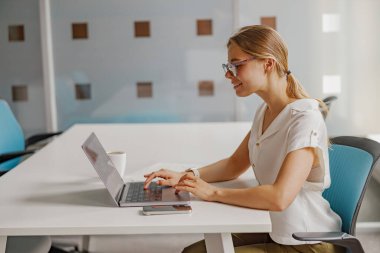 Çağdaş bir çalışma alanında dizüstü bilgisayar kullanan odaklanmış bir kadın üretkenliği ve profesyonelliği somutlaştırıyor..