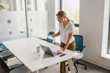 Odaklanmış ve kararlı bir kadın, şık bir ofis masasında laptopu ve çeşitli belgelerle yoğun bir şekilde işbirliği yapıyor.