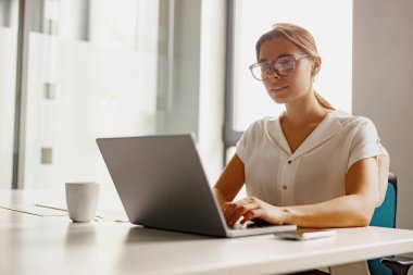 Odaklanmış ve kendini işine adamış profesyonel bir kadın özenle dizüstü bilgisayarı üzerinde çalışıyor.