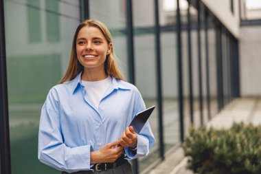 Neşeli genç bir kadın, modern profesyonelliğin bir örneği olarak şık bir ofis ortamında bir tablet tutuyor..
