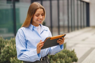 Bir tabletle meşgul neşeli genç bir kadın şehir ortamında modern teknoloji etkileşimi sergiliyor..