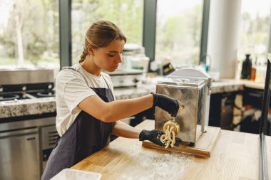 Güzel, parlak ve modern bir mutfak ortamında genç bir kadın makarnayı ustalıkla pişirir.