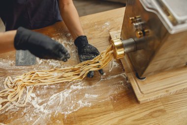 Uzman eller makarnayı ustalıkla bir makine kullanarak yapıyor, ev yemeklerinin güzel sanatını vurguluyor.