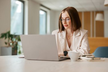 Kendini işine adamış ve işine odaklanmış profesyonel bir kadın modern ve şık bir ofis alanında özenle dizüstü bilgisayarı üzerinde çalışıyor.