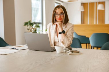 Profesyonel iş kıyafeti giymiş odaklanmış bir kadın modern ofis ortamında özenle dizüstü bilgisayarı üzerinde çalışıyor.