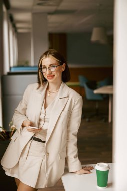 Kendine güvenen, şık, profesyonel bir kadın duruşunu sergilemek için modern ve çağdaş bir çalışma alanında zarifçe poz veriyor.
