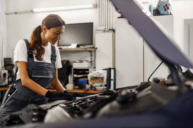 Kendini adamış ve yetenekli bir tamirci modern bir oto tamir atölyesi ortamında motoru dikkatle inceler.