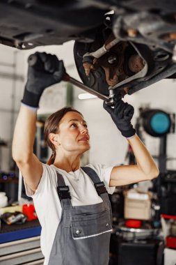 Becerikli bir kadın, iyi döşenmiş bir otomobil tamirhanesinde bir aracı tamir etmek için İngiliz anahtarını ustalıkla kullanır.