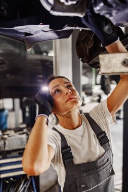 Kendini işine adamış, araç bakımında uzman bir tamirci detaylı incelemeler yapmak için el feneri kullanır.