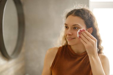 Genç bir kadın şık ve modern bir banyo ortamında derisi için pamuk pedi kullanıyor.