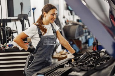 Çok yetenekli ve bilgili bir kadın tamirci düzenli bir garajda araba motorunu dikkatle inceliyor.