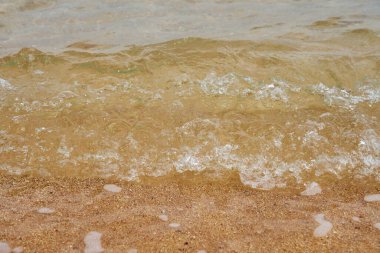Kumlu sahilde deniz suyu. Suda kabarcıklar.