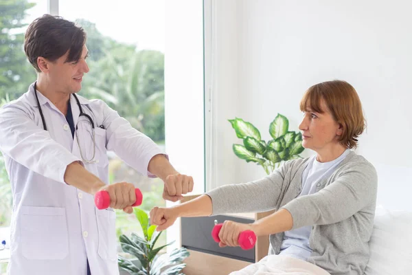 Female patient exercising with dumbbells in the hospital. Physiotherapist Assisting Senior Woman To Lift Dumbbells. the doctor is examining the patient in the hospital