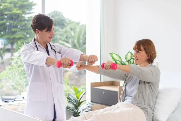 Female patient exercising with dumbbells in the hospital. Physiotherapist Assisting Senior Woman To Lift Dumbbells. the doctor is examining the patient in the hospital