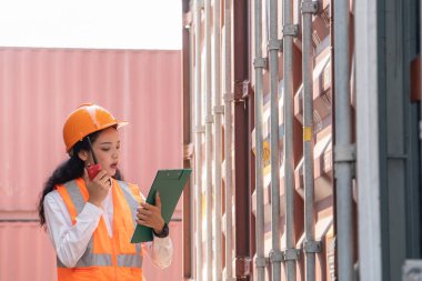 Professional asian female workerusing walkie-talkie in shipping yard industrial container  box from cargo freight ship for import export. Logistic, transportation