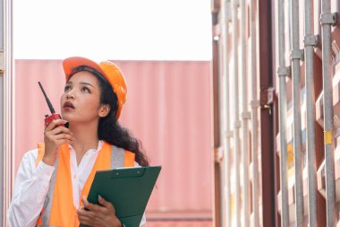 Professional asian female workerusing walkie-talkie in shipping yard industrial container  box from cargo freight ship for import export. Logistic, transportation