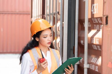 Professional asian female workerusing walkie-talkie in shipping yard industrial container  box from cargo freight ship for import export. Logistic, transportation