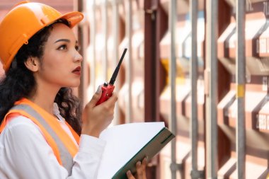 Professional asian female workerusing walkie-talkie in shipping yard industrial container  box from cargo freight ship for import export. Logistic, transportation