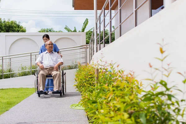 Nursing Home Care concept. asian Young nurse disabled elderly man. Nurse, care home and elderly man with disability in a wheelchair in an outside medical facility.