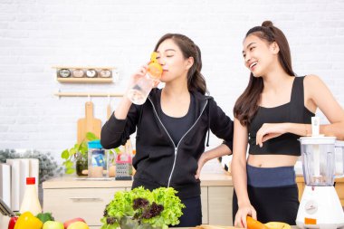 Spor giyim sektöründe aktifleşen Asyalı iki kadın mutfakta sağlıklı yiyecekler yiyor..