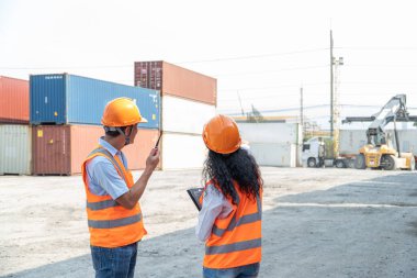 Güvenlik yeleği ve kask giyen iki Asyalı sanayi mühendisi ve kadın. Foreman, Endüstriyel Konteyner Kargo 'da çalışan işçi ya da işçiyle konuşuyor..