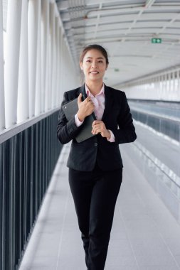 young Asian businesswoman in black suit using digital tablet and standing on walkway station with copy space.