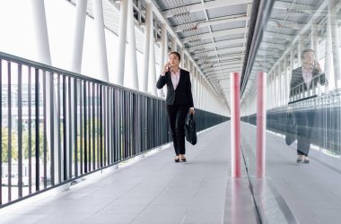 young Asian businesswoman in black suit using digital tablet and standing on walkway station with copy space.