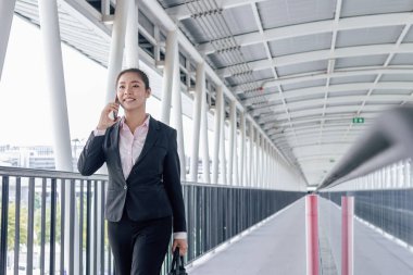 young Asian businesswoman in black suit using digital tablet and standing on walkway station with copy space.