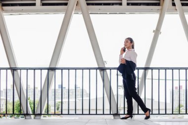young Asian businesswoman in black suit using digital tablet and standing on walkway station with copy space.