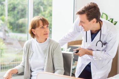 Kafkasyalı erkek doktor, tekerlekli sandalyedeki yaşlı kadın hastayı muayene ediyor..