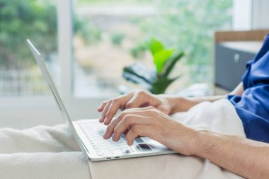 Hastane odasında dizüstü bilgisayar kullanan beyaz bir hasta. Hasta bir adam hastane yatağında yatıyor..